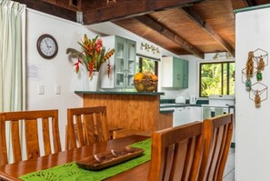 Enjoy meals in this inviting dining area with a table and chairs, surrounded by a kitchen with a view of lush greenery.