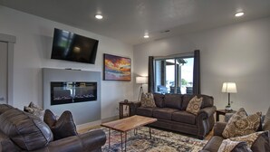 A modern living room with leather sofas, a wooden coffee table, a flat-screen TV, and a large window offering a view of the outdoors.