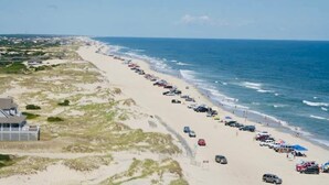 Uma praia com uma fileira de carros estacionados e um edifício à esquerda.