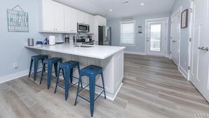 Uma cozinha moderna com armários brancos, uma ilha central com banquetas, micro-ondas e geladeira.