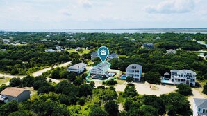 Vista aérea de uma área residencial costeira com várias casas, uma piscina e acesso à praia.