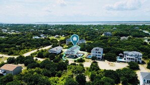 An aerial view of a coastal residential area with multiple houses, a swimming pool, and a beachfront.