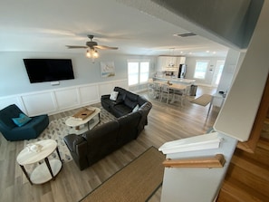 A spacious living area with a large black sofa, a blue armchair, and a flat-screen TV mounted on the wall.