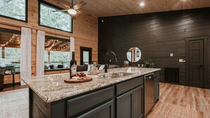 A modern kitchen with a large island, dark wooden walls, and a large window overlooking the outdoors. -  Smoky Mnt Couples Cabin / Hot Tub / Secluded but close to local shops (Sevierville)