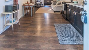 A spacious living area with a wooden ceiling, a dining table with chairs, a sofa, and a kitchen area with cabinets and a countertop.