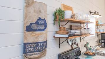 Una cocina con un letrero en la pared que indica semillas híbridas cultivadas en Kentucky, estantes con utensilios de cocina y una estufa.
