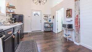A spacious kitchen with dark wood flooring, a chandelier, and a white door.
