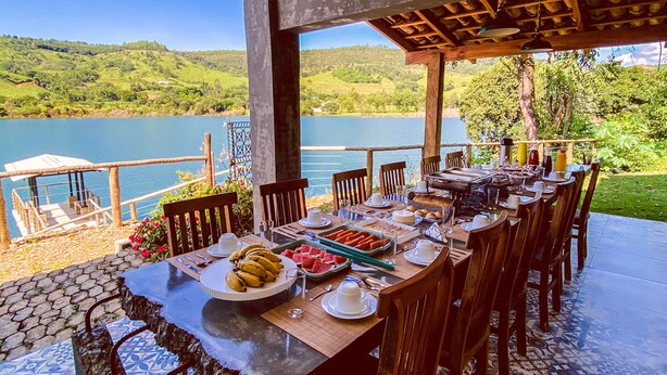 A dining area with a view of a lake, wooden furniture, and a tiled floor. - Bica D'água Boutique Hotel (Capitólio)