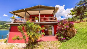 A two-story building with a red facade, a balcony with wooden railings, and a glass door entrance. - Bica D'água Boutique Hotel (Capitólio)