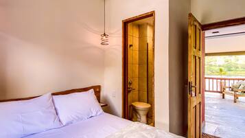 A hotel room with a large bed, a hanging light fixture, a bathroom door, and a view of the outside balcony.