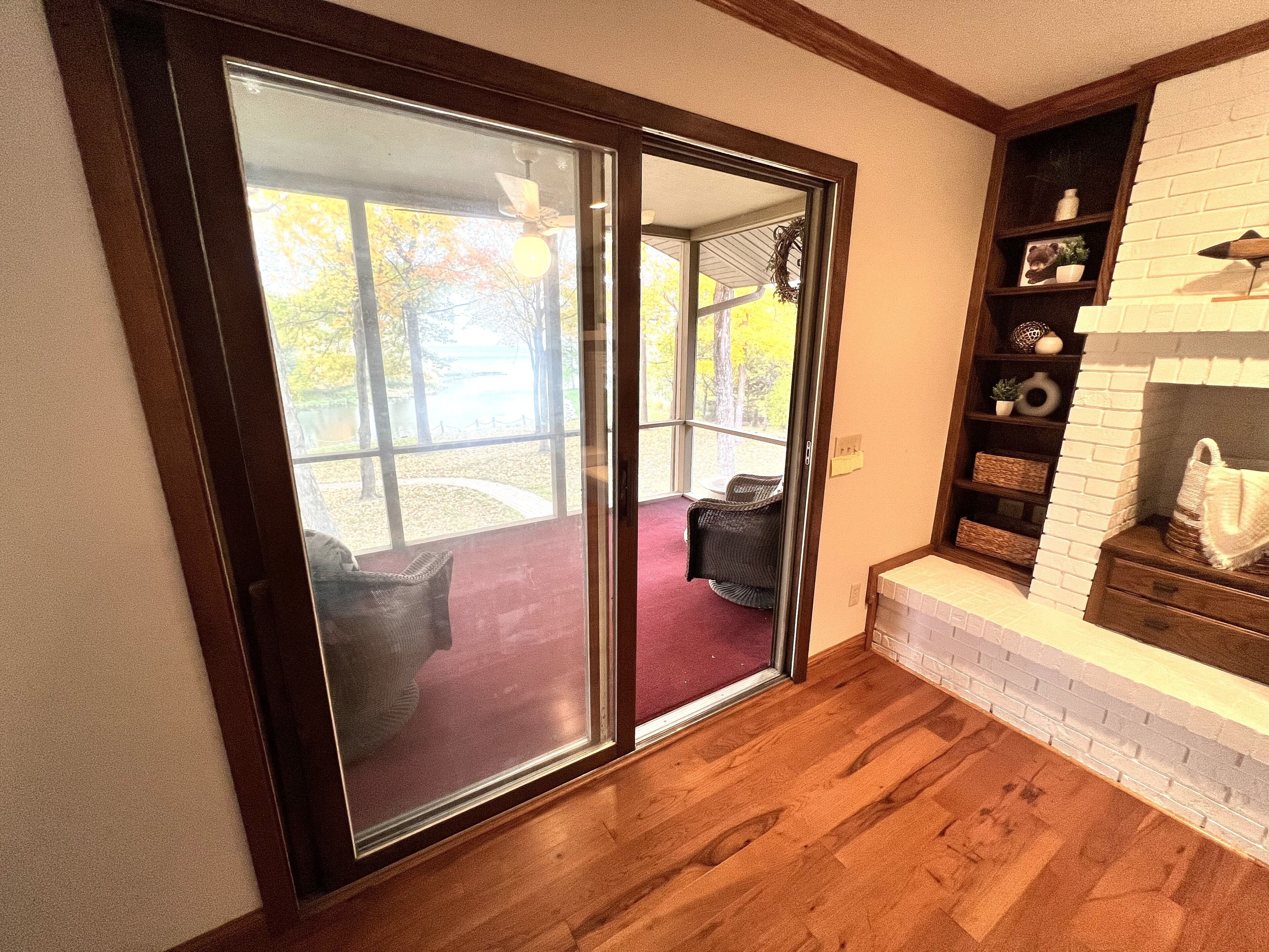 Une pièce dotée d’un plancher en bois, d’une cheminée et d’une porte-fenêtre coulissante donnant sur un espace extérieur avec une terrasse et une vue sur les arbres.