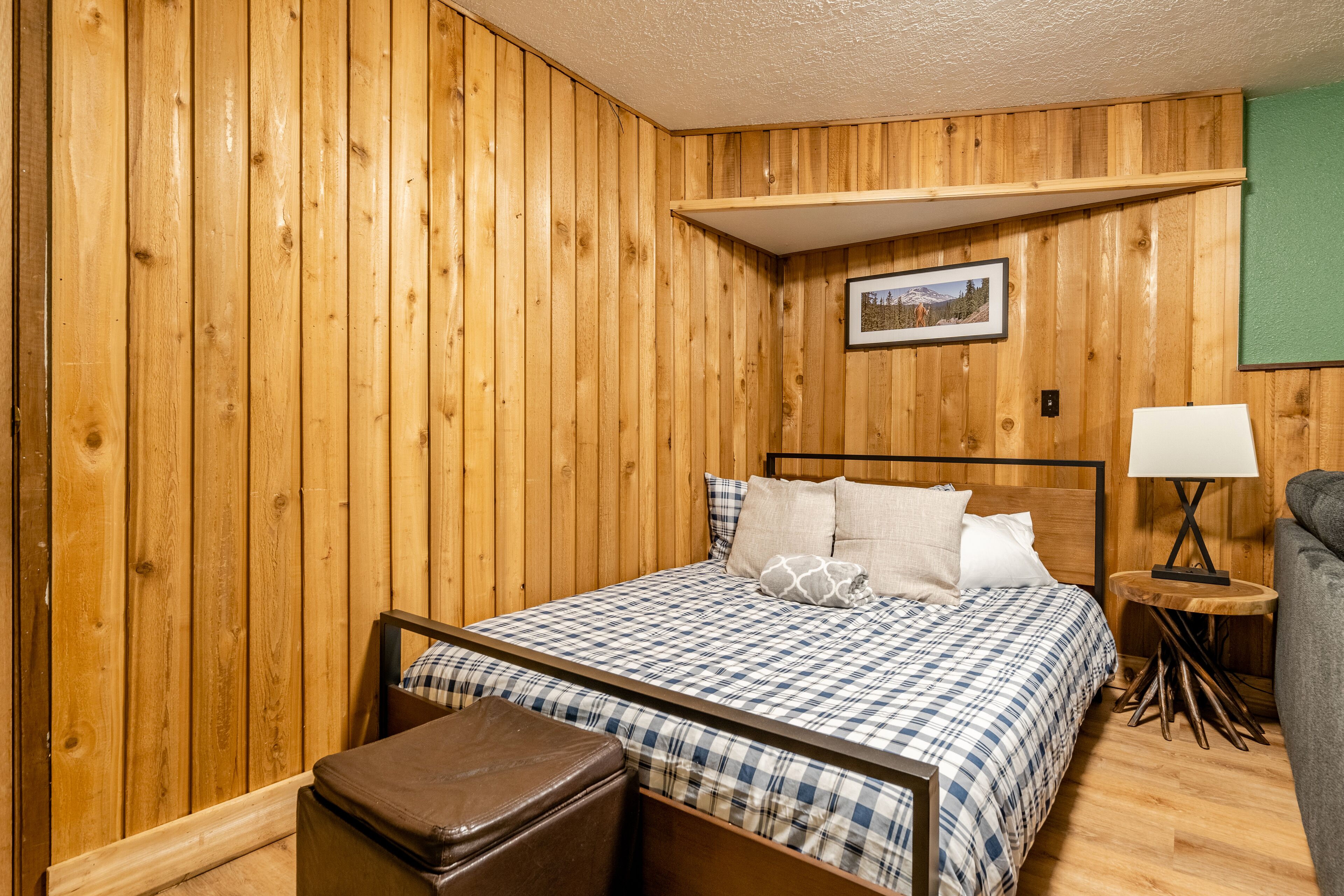 Una habitación con paneles de madera, una cama, una mesita con lámpara y un banco.