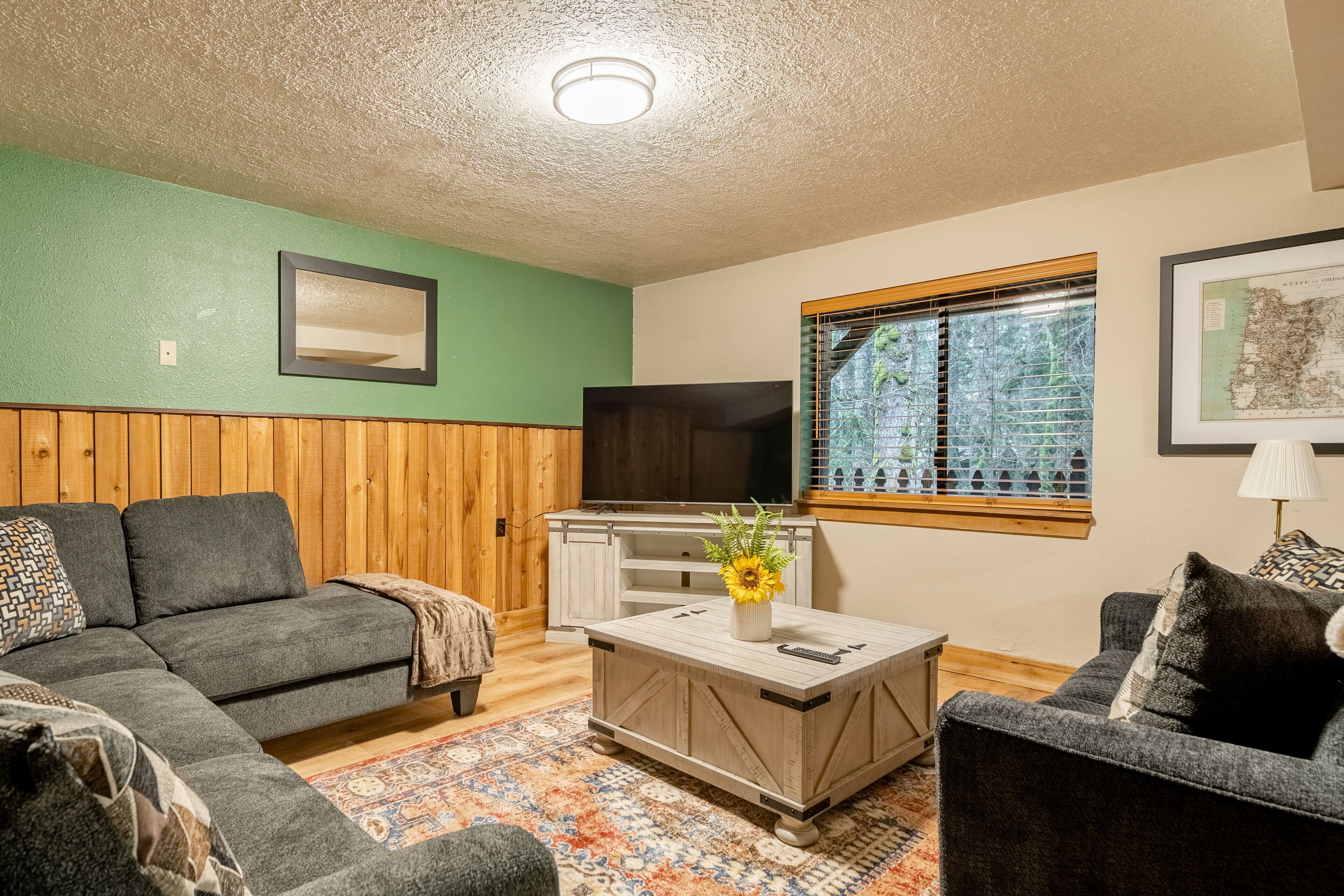 A living room with a sectional sofa, a coffee table with a vase, a television, and a window with blinds.