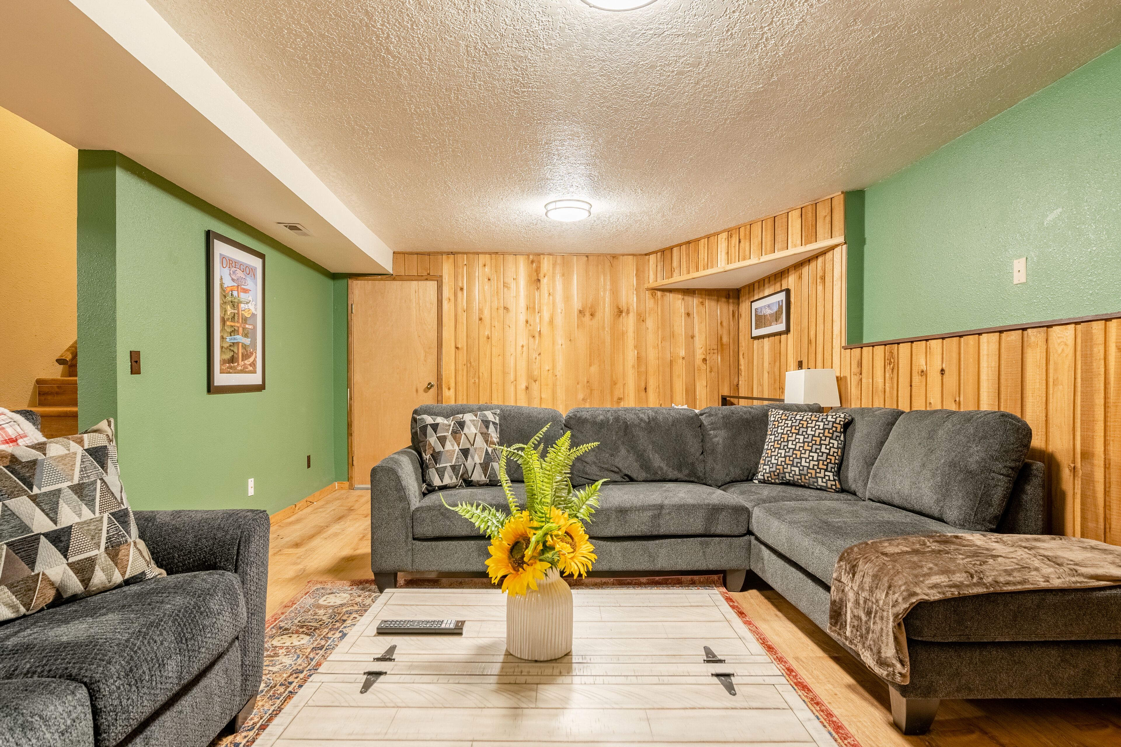 A living room with a sectional sofa, a coffee table with a vase of flowers, and a patterned rug.