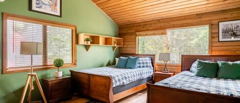 A bedroom with two wooden beds, a green wall, and large windows.