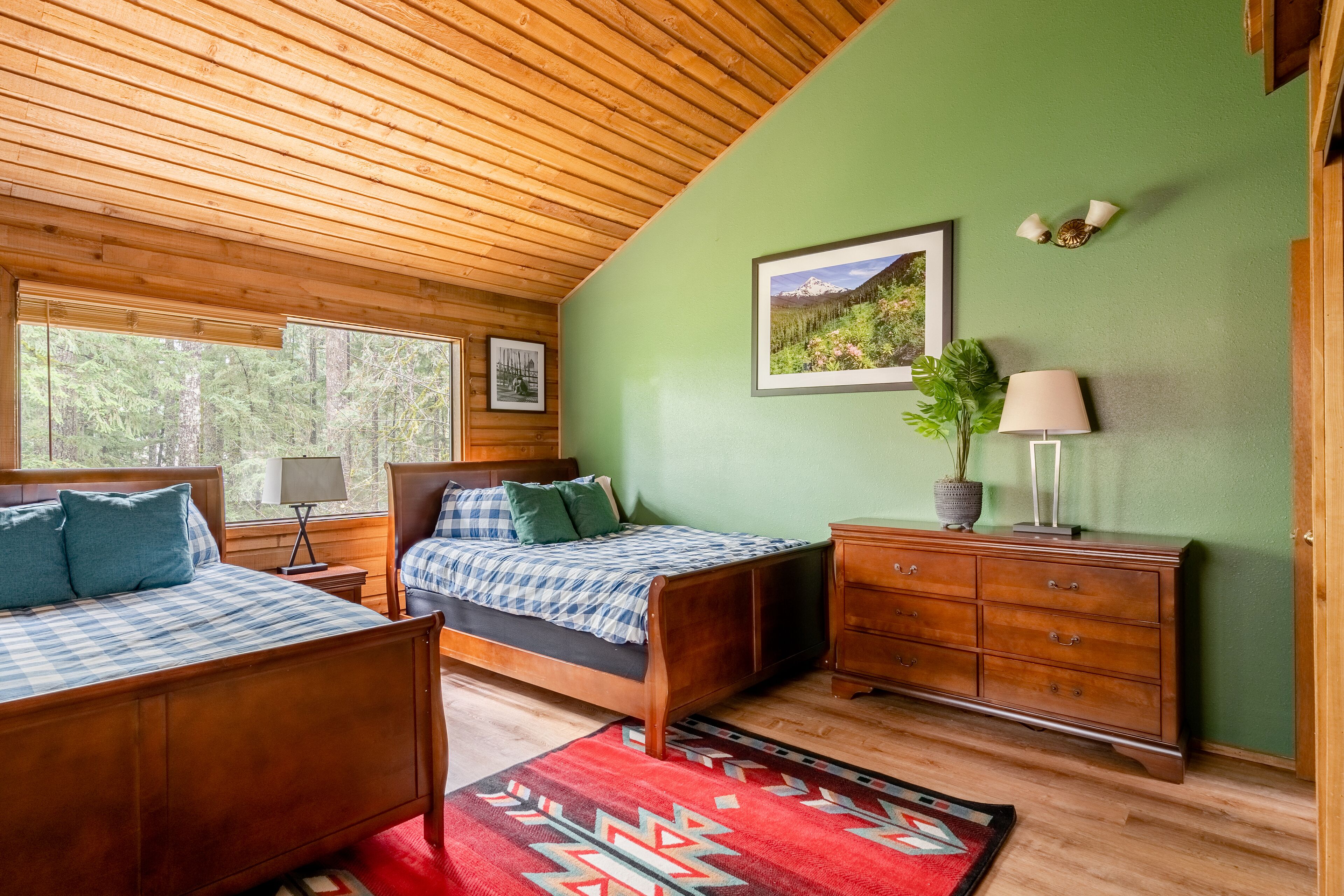 Une chambre dans un chalet en bois, avec deux lits, une commode, une lampe et un tableau encadré au mur.