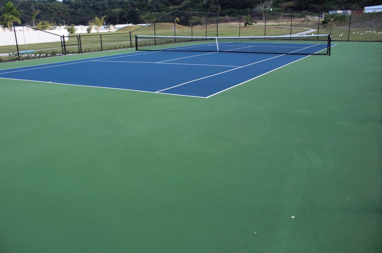 En tennisbana med nät, omgiven av ett staket och grönska.
