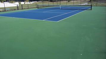 En tennisbana med nät, omgiven av ett staket och grönska.