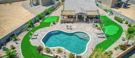 An aerial view of a residential area with a swimming pool, green lawns, and a house with a tiled roof.
