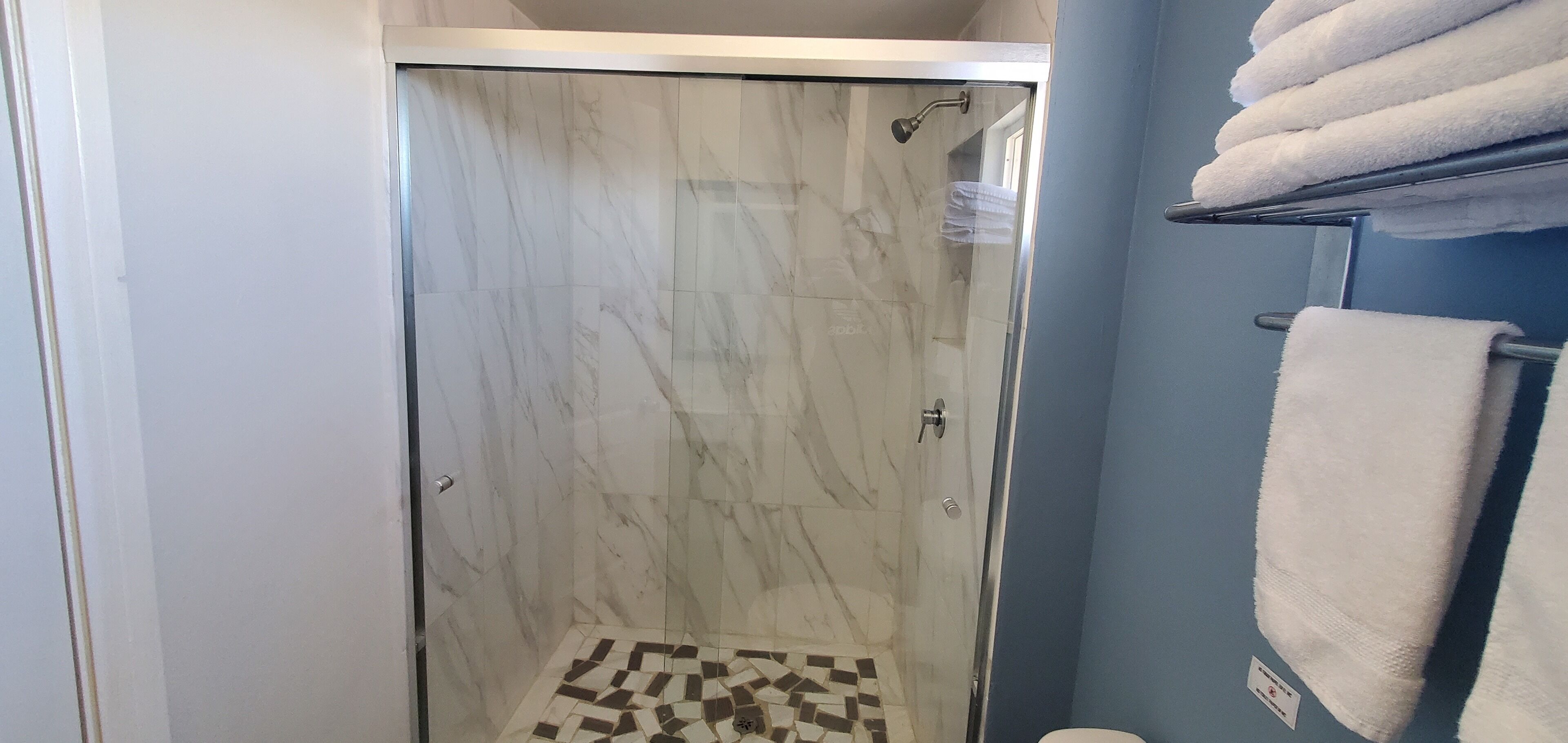 A shower area with a glass door, a tiled floor, and a towel rack with towels.