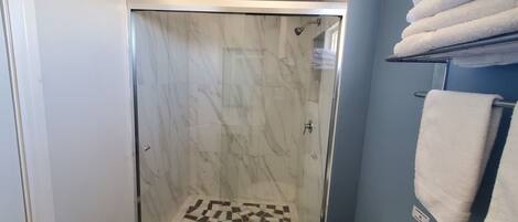 A shower area with a glass door, a tiled floor, and a towel rack with towels.