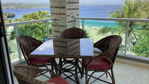 Un balcon avec des fauteuils en osier et une table, offrant une vue sur la plage et l’océan.