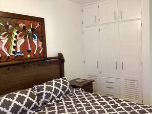 Un dormitorio con cama, cabecera de madera, armario con múltiples puertas y un cuadro de colores en la pared.
