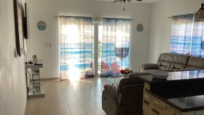 Un grand espace de vie comprenant un canapé, une table basse et une table à manger. Il y a un ventilateur de plafond et une vue à travers les portes vitrées.