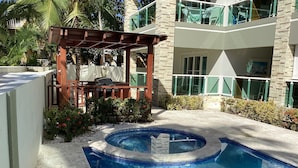 Une piscine avec un bord carrelé, une pergola en bois et un bâtiment doté d’un balcon.