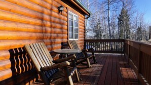 Une cabane en bois dotée d’une terrasse, de deux fauteuils Adirondack et d’une table.