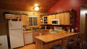 Une cuisine avec des meubles en bois, un réfrigérateur, un four à micro-ondes, un évier et un îlot central en bois doté de tabourets de bar.
