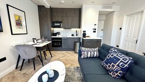 Een moderne woonkamer met een donkerblauwe bank, een marmeren salontafel en een eethoek met een witte tafel en grijze stoelen.