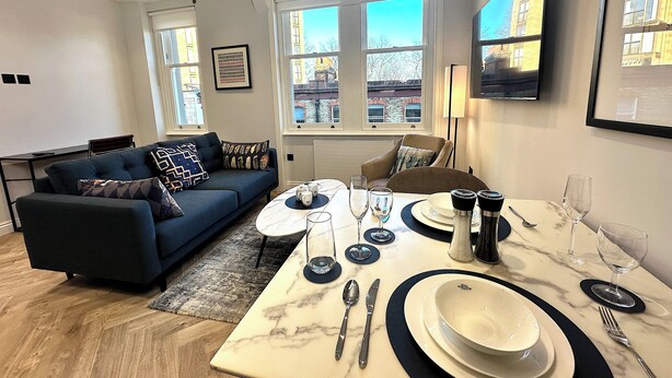 Een moderne woonkamer met een bank, salontafel en eethoek, compleet met borden, glazen en bestek.