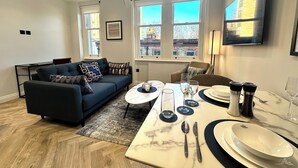 Een moderne woonkamer met een bank, een eettafel voor vier personen en grote ramen met uitzicht op de stad.
