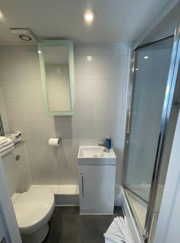 A compact bathroom with a toilet, a sink, and a shower area. - Chiltern Street Apartments - Deluxe (London)