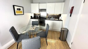 Una cucina compatta con mobili bianchi, un tavolo da pranzo in vetro e una sedia grigia.