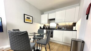 Una cucina compatta con mobili bianchi, un lavello in acciaio inossidabile e un piccolo spazio pranzo con due sedie.