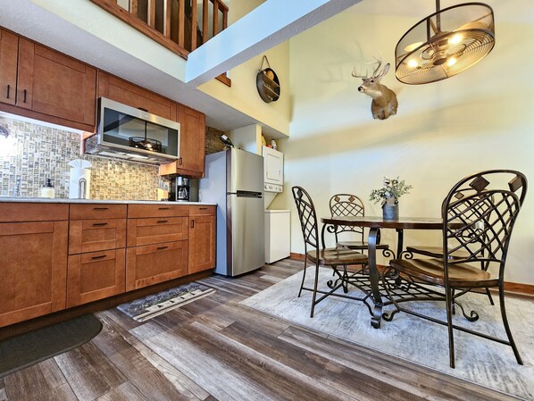 A kitchen with wooden cabinets, a stainless steel refrigerator, a dining table with metal chairs, and a wall-mounted deer head decoration.