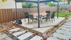 Un patio couvert, équipé d’une table et de chaises, entouré d’une terrasse en bois et d’une clôture en bois.