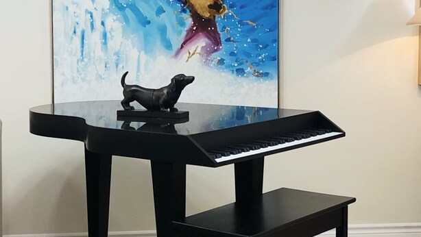 Un piano doté d’un pupitre noir et surmonté d’une petite figurine de chien, placé devant un tableau.