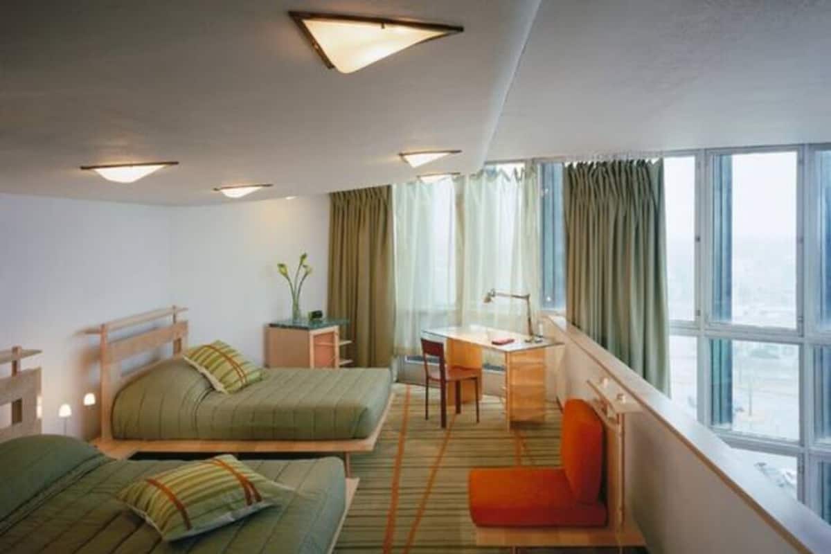 A hotel room with two beds, a desk, a chair, and a large window with curtains.