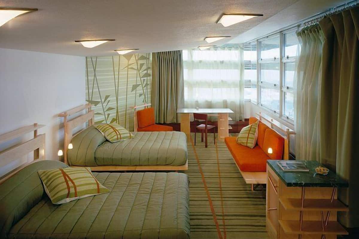 A compact hotel room with two single beds, a small dining table, and a sofa.