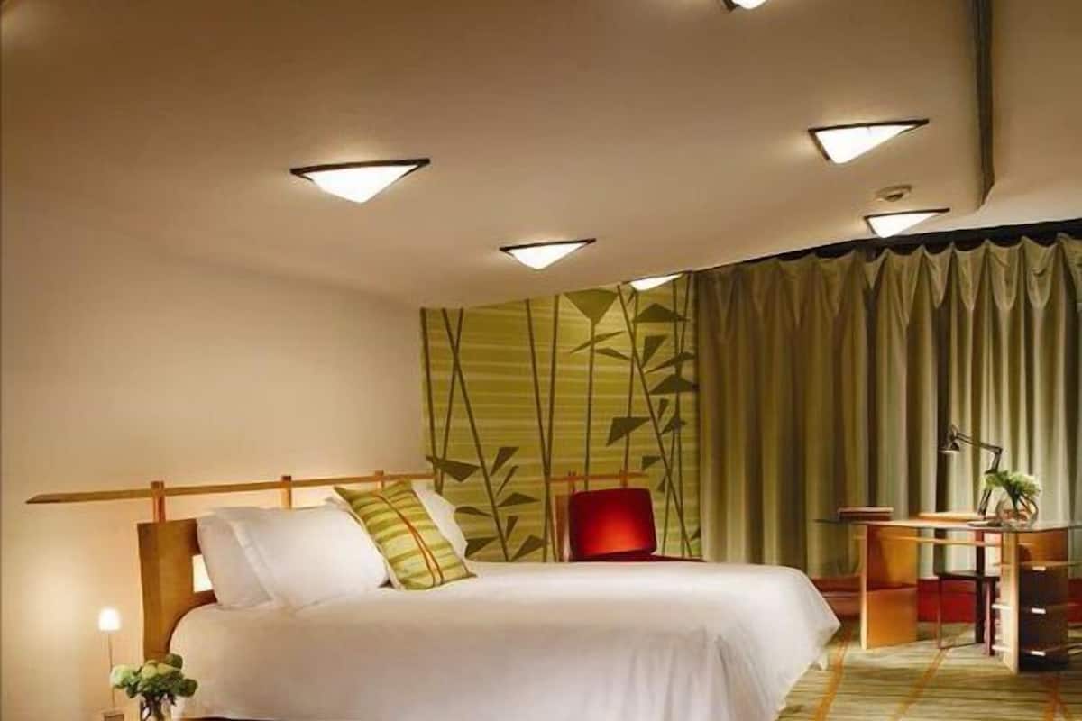 A modern hotel room with a large bed, a desk, and a red sofa.