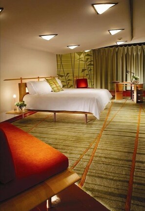 A modern hotel room with a large bed, a desk, and a red sofa.