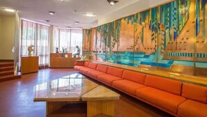 En moderne lobby med en lang, orange sofa, et glasbord og et farverigt, abstrakt vægmaleri.