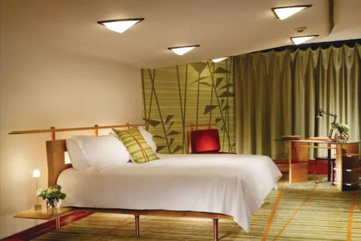 A hotel room with a bed, a desk, and a chair. There is a curtain with a bamboo pattern on the wall.