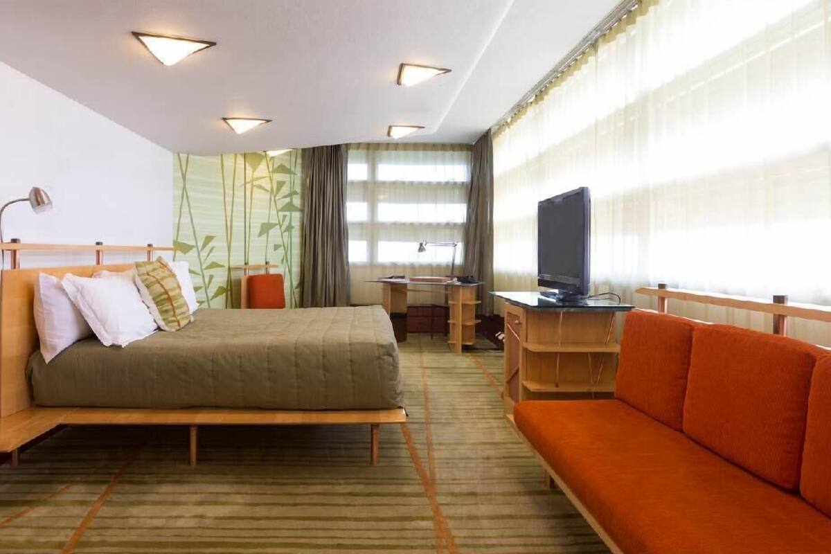 A hotel room with a bed, a desk with a computer, a TV, and a sofa.