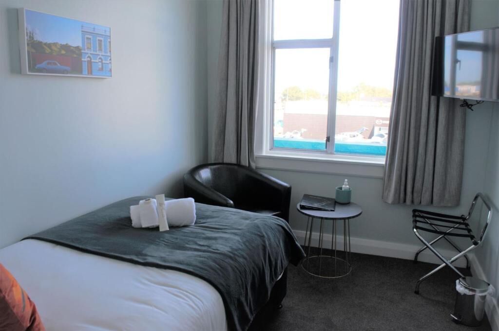 Ein Hotelzimmer mit Bett, kleinem Tisch, Stuhl, Fernseher und einem Fenster mit Vorhängen.