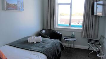 Ein Hotelzimmer mit Bett, kleinem Tisch, Stuhl, Fernseher und einem Fenster mit Vorhängen.