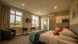 Una habitación de hotel con cama, escritorio, silla, televisión y kitchenette.
